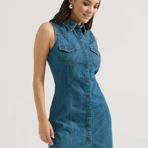 A woman in blue denim dress standing next to wall.